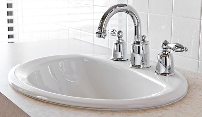 Clean white ceramic bathroom sink with chrome faucet and two handles on a countertop
