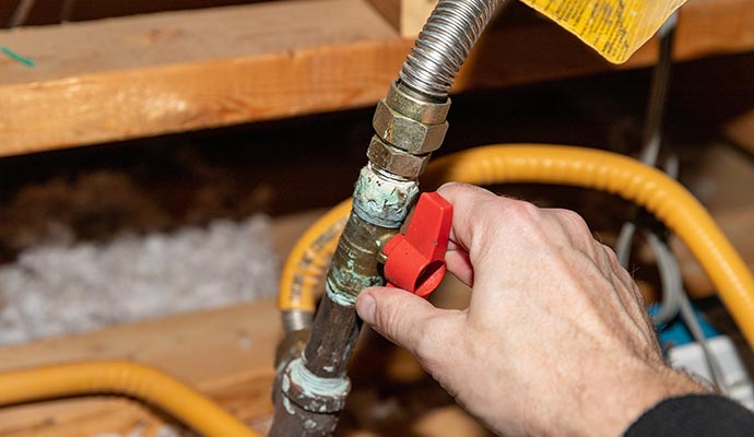 Expert operating a red valve on a corroded metal pipe with attached flexible hoses