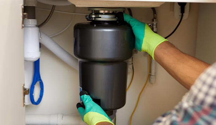 A professional installing a black garbage disposal unit under a kitchen sink