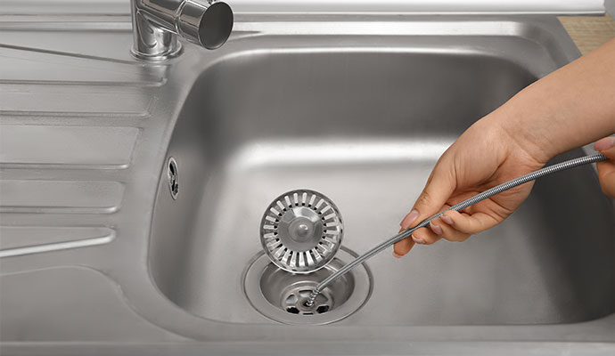 Hand Clearing a Clogged Drain Pipe in a Sink