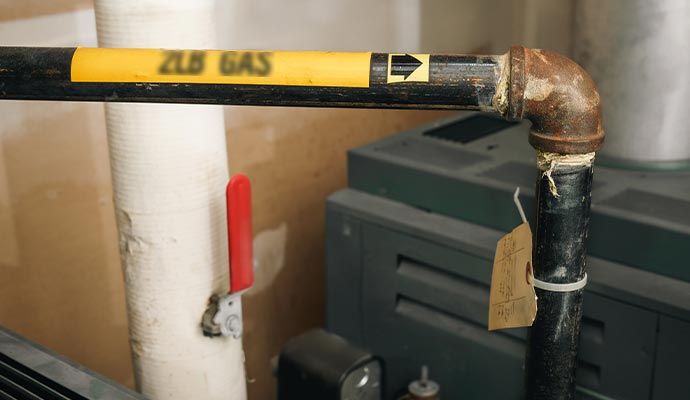 Gas pipe in an industrial utility room showing a rusted elbow joint and a red-handled valve