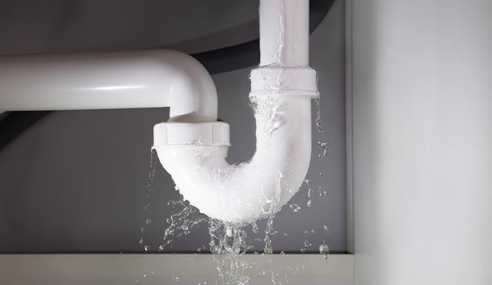 White PVC drain pipe under a sink leaking water from the joints