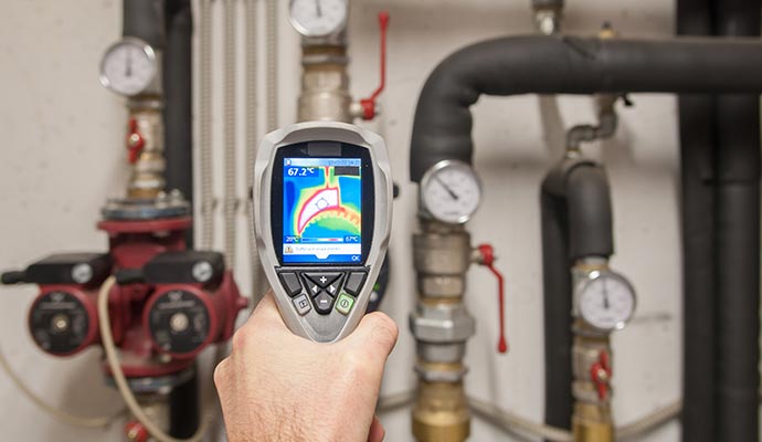 Professional technician using a handheld device to inspect pipes and gauges for possible leaks