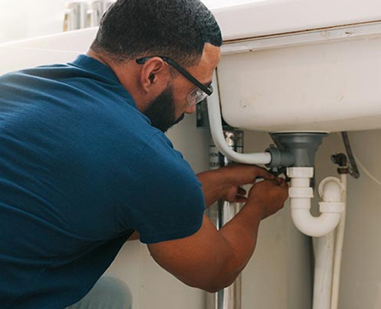 Plumber in blue shirt and safety glasses working under a sink with tools