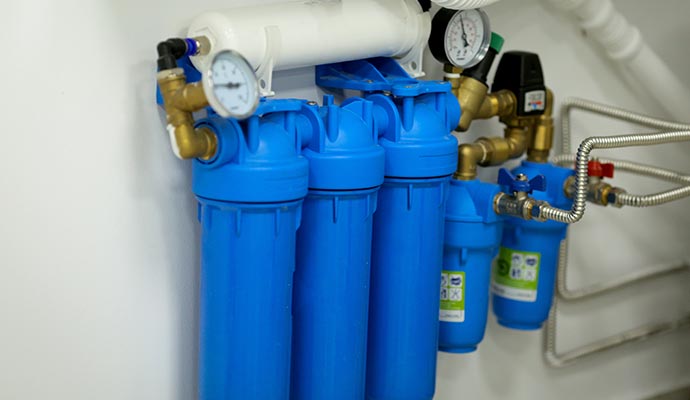 Multi-stage water filtration system with blue filter housings and pressure gauges mounted to a wall