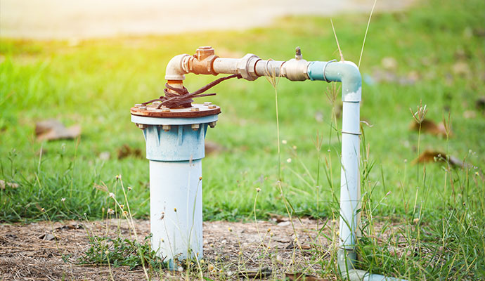 Outdoor water well casing pipe and head in a sunny grassy yard