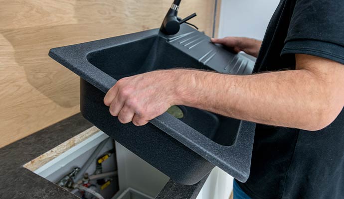 Plumber replacing modern black kitchen sink