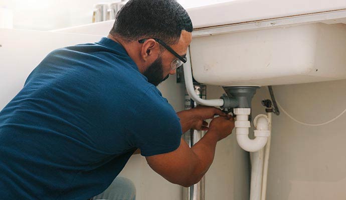 Plumber repairing broken pipe under sink